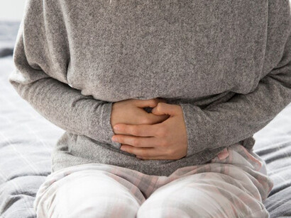 A sick woman with food intolerances sitting in bed, clutching her stomach in pain from food allergies