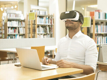Wearing VR goggles in the library, the student visualises how the brain continuously updates and processes information, akin to how artificial intelligence adapts to the real world through sensors and algorithms