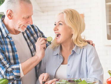 Evoke the warmth of family and healthy living with a portrait of a senior man watching his wife cut vegetables in a modern kitchen, showcasing the joys of cooking together and promoting a wholesome lifestyle