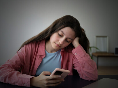 A girl holding her phone, appearing despondent, highlighting the link between excessive social media use, feelings of loneliness, and the pressure of unrealistic comparisons