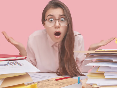 A young brunette student grapples with information overload and the data deluge while sitting at her desk surrounded by books