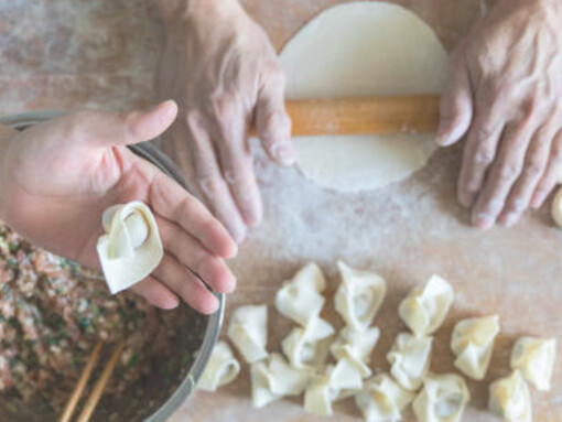 Two hands delicately open the manti, carefully filling it with seasoned minced meat