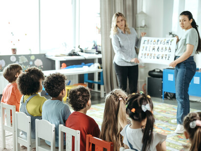 Two female teachers holding up a sign of the alphabet letters to young children