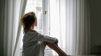 Young woman sitting on a sofa at home, looking out the window