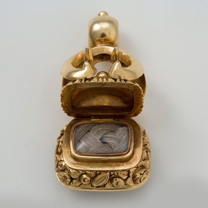 Este reloj victoriano se abre para revelar mechones trenzados de cabello humano. La piedra de su base es muy oscura, casi negra. Estas características son típicas de las joyas de luto