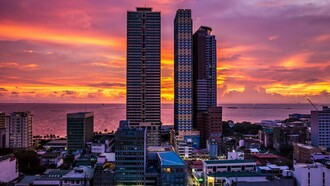 Towering buildings overlooking Manila Bay at dusk, symbolising a city that remains open to history, hope, and endless becoming