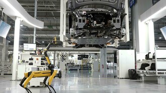 Un robot quadrupede di Boston Dynamics ispeziona una linea di assemblaggio automatizzata in una fabbrica high-tech, simbolo della trasformazione postindustriale e della crescente automazione dei processi produttivi