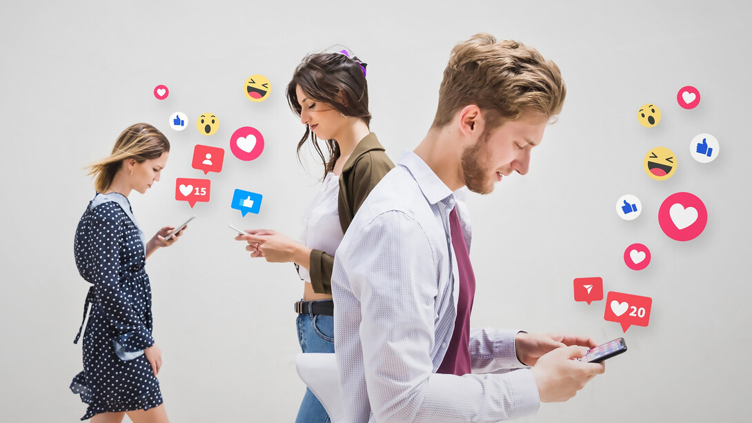 A group of people walking on the pavement, each absorbed in their phones, illustrating the addictive nature of social media