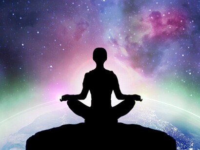 From behind, a woman is seen meditating, her focus drawn to the infinite stars and galaxies of the universe unfolding in front of her