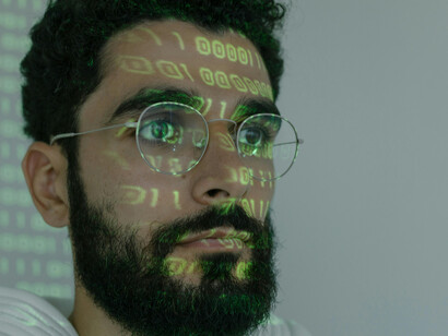 Hombre con unos y ceros reflejados en su rostro. La tecnología detrás de los deepfakes se basa en una combinación de inteligencia artificial y aprendizaje automático