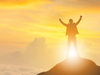 In silhouette, a businessman exults in success, finding happiness atop a mountain at sunset