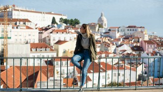 A woman sitting on metal railings and watching the scenery in Lisbon, Portugal