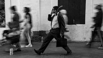 A focused man moving through a blur of rushing pedestrians, representing the modern pressure to stay constantly occupied