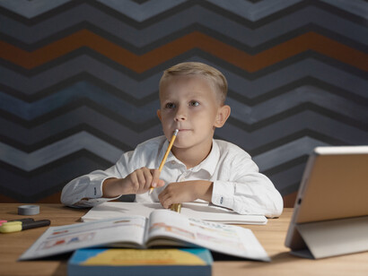 Criança faz tarefa da escola com livro físico e tablet com recursos digitais