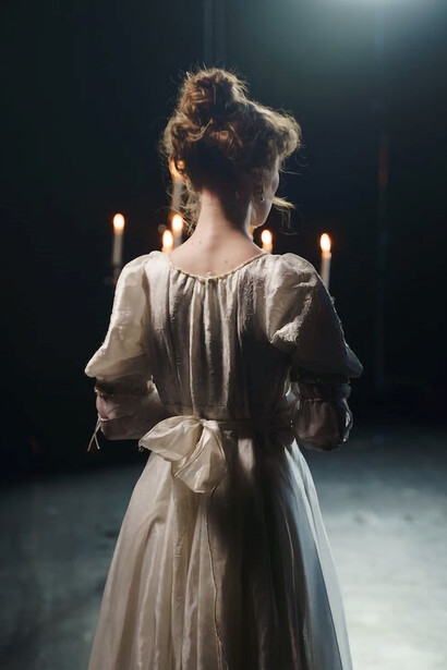 A woman seen from behind, elegantly grasping a candelabrum on a theater stage