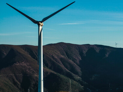 A wind turbine, against a mountain backdrop and a clear, blue sky