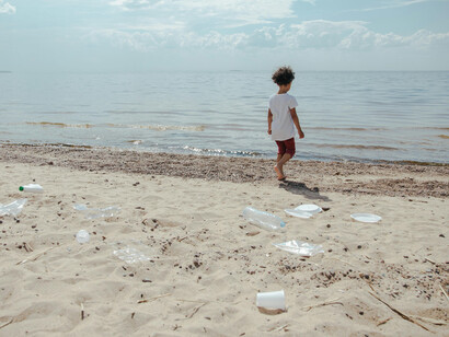 A child walks towards the sea on a beach, littered with dirt