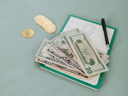 A checkbook, a hanful of US dollar bills and physical representations of Bitcoins