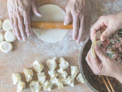 Two hands gently part the manti dough, expertly filling it with savory minced meat