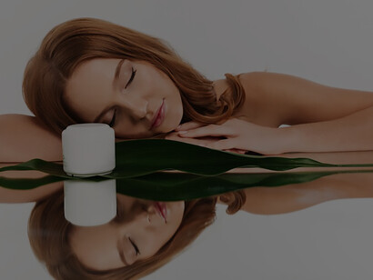 Experience luxurious skincare indulgence as a ginger woman with long hair reclines gracefully on a mirrored table, showcasing a coveted bottle of body cream