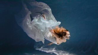 A graceful body suspended in water in a flowy white dress, conveying a weightless, unhurried state that mirrors emotional release