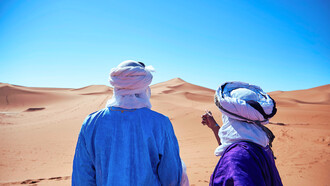 Two travellers gazing across the desert in M'hamid El Ghizlane, representing the quiet allure of the Sahara’s vast and timeless horizons