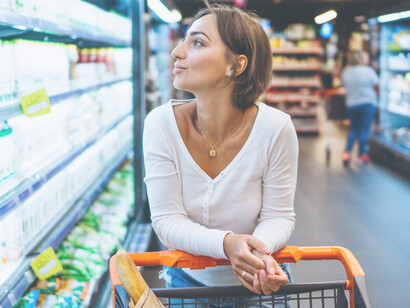 A woman inspects products by the refrigerator while shopping for groceries