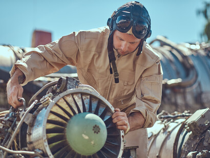 A pilot-mechanic in uniform and flying helmet, repairing the dismantled airplane turbine