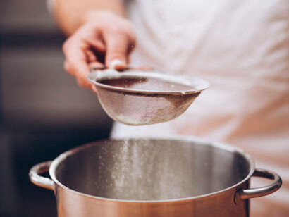 A hand carefully sifts flour through a sieve, illustrating the concept of a filtration system