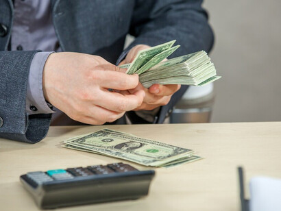 A young businessman working from his office, counting cash, embodying corporate greed