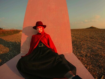A woman wearing a long black dress and red top with a fashionable hat sitting in the middle of a field for the ideal social media pose