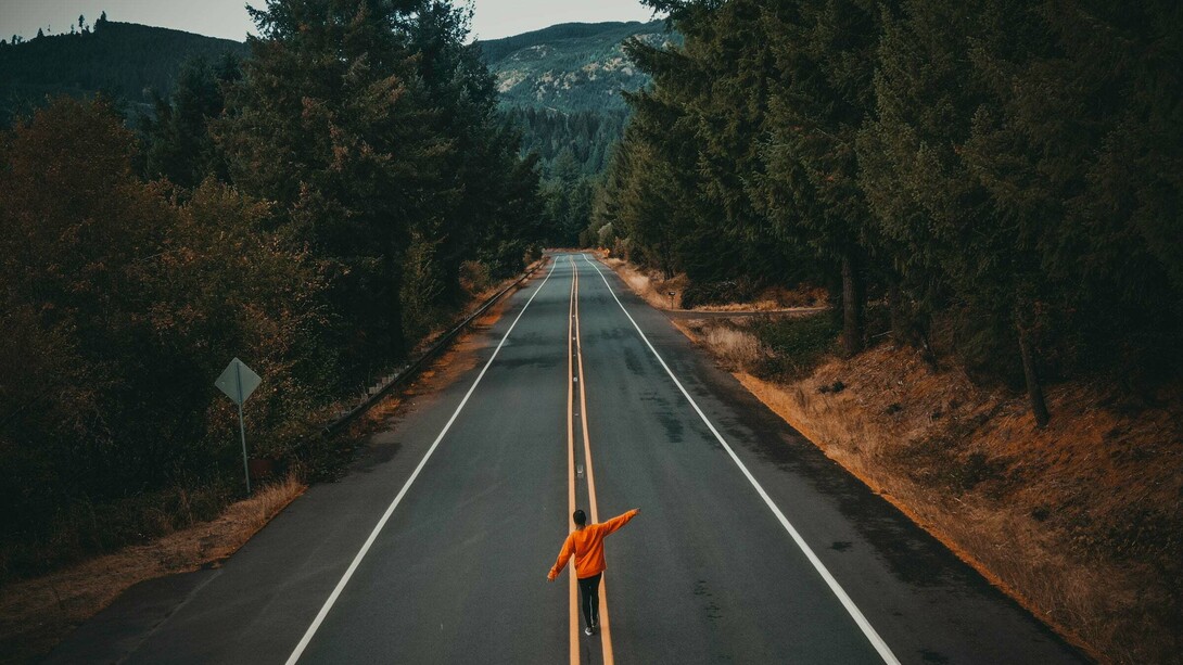 A person balancing their arms while walking through the middle of a forest road