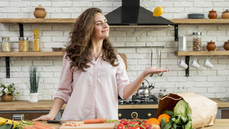 A brunette woman stands in the kitchen surrounded by healthy food