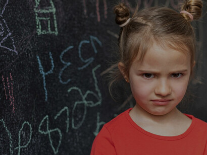 A young girl, showing signs of dysregulation, stands by a blackboard in a classroom setting
