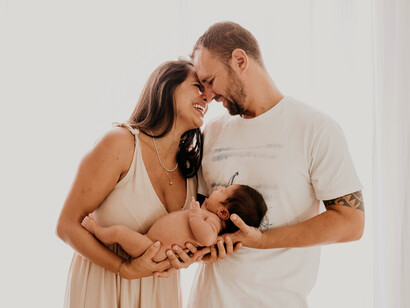 Una pareja sonriente sostiene a su bebé recién nacido. La familia es la unidad de la sociedad y como tal interactúan dentro de la sociedad