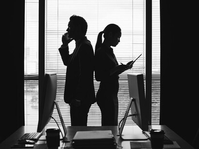 Dark silhouettes of a man and woman in business attire standing by a window in a modern office, symbolizing professional collaboration